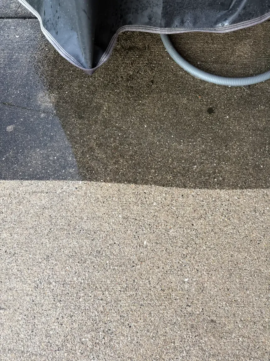 A concrete slab part-way through a wash: the top half still dark with dirt, the bottom half cleaned back to pale concrete, with a straight line between them.